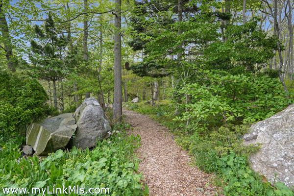 An enchanting, woodchip-lined path meanders through majestic glacial boulders, offering a direct invitation to explore the surrounding conservation land
