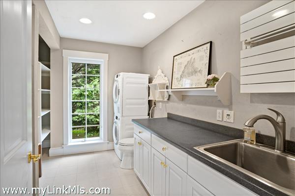 Bright and spacious laundry room featuring a long expanse of counter space, extensive cabinetry for organization, a dedicated utility sink, and a stacked washer and dryer setup
