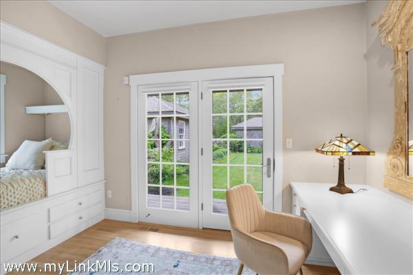 A bright and captivating bedroom featuring a custom arched built-in bed alcove with integrated under-bed storage drawers, a seamless built-in desk workstation, and double glass doors that open directly to the outside