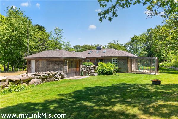 The scenic side yard is beautifully terraced with classic New England stone walls, creating a manicured backdrop that seamlessly blends with the natural woodland surroundings
