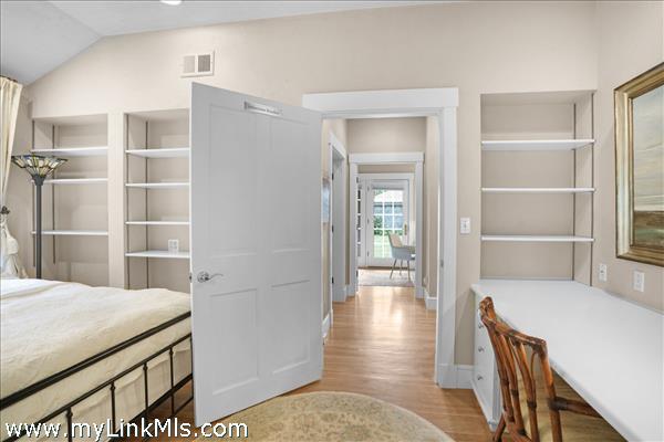 A bright and airy secondary bedroom featuring expansive custom built-in shelving, an integrated study desk, and large windows that fill the space with natural light