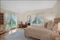 The sun-drenched primary bedroom serves as a private sanctuary, featuring expansive windows, elegant drapery, and French doors that open directly to a tranquil outdoor deck